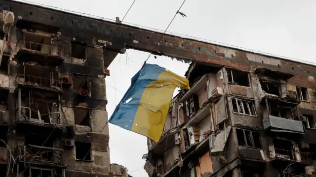 一面破损的乌克兰国旗悬挂在两栋遭炸弹破坏的建筑物之间
