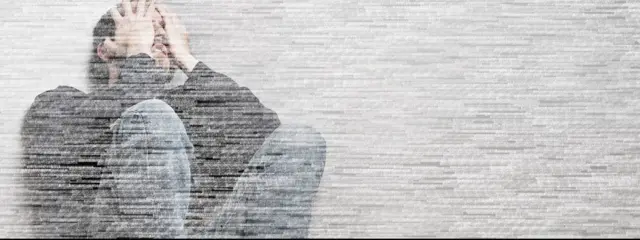 လူတစ်ယောက် အခန်းထောင့်မှာ ထိုင်နေတာကို မှုန်ဝါးအောင် ပြုပြင်ထားတဲ့ပုံ