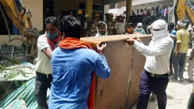 ఇల్లు కూల్చడానికి ముందు సామాన్లను బయట పెడుతోన్న కార్మికులు