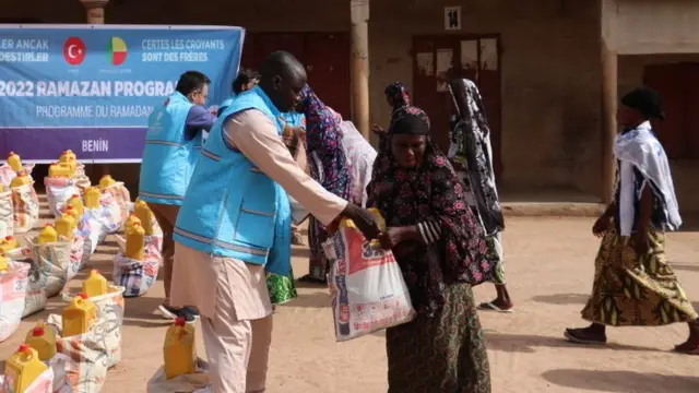 Des personnes reçoivent des colis d'aide alimentaire distribués par la Fondation religieuse turque dans le jardin d'une école à Djougou, au Bénin, le 05 avril 2022