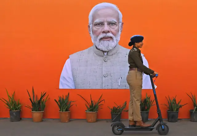A police officer rides an electric scooter past a poster of Indian Prime Minister Narendra Modi in Ahmedabad, January 2024
