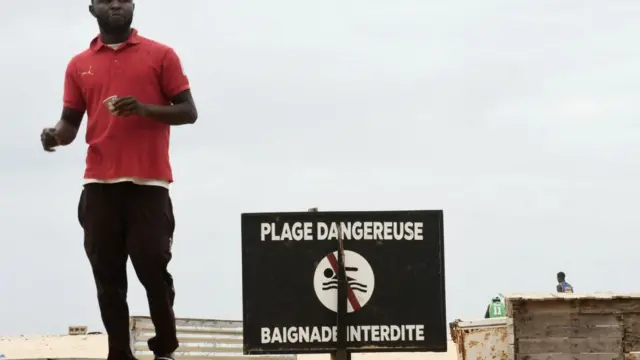 Un homme passe devant un panneau indiquant "plage dangereuse, à Dakar.