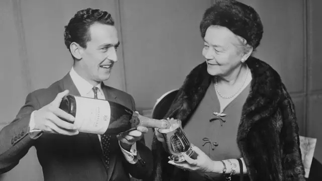Lily Bollinger es servida champán por el jockey inglés Josh Gifford, en el hotel Savoy de Londres 1968