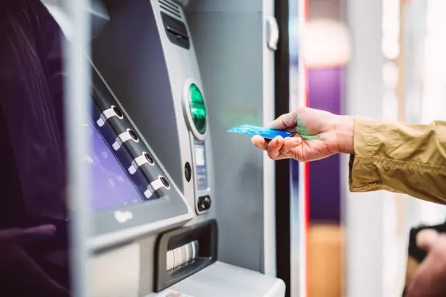 Female hand inserting bank card into automatic cash machine