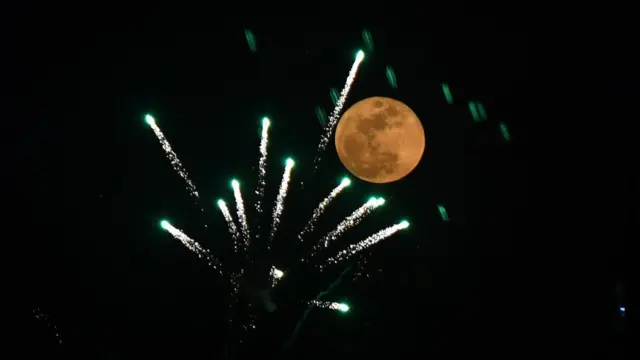 在北京，市民燃放的烟花与月圆相映