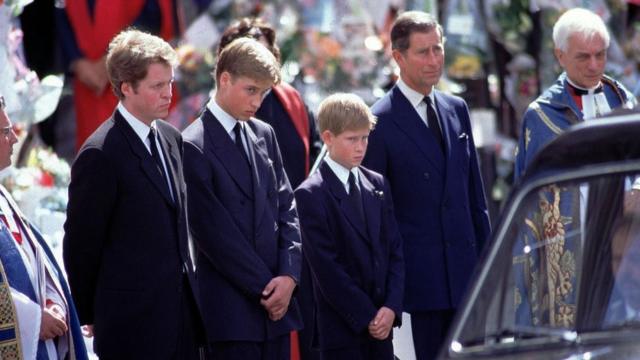 El príncipe Harry, entre su padre, el príncipe Carlos, y su hermano, el príncipe William, viendo pasar el coche fúnebre con los restos de su madre.