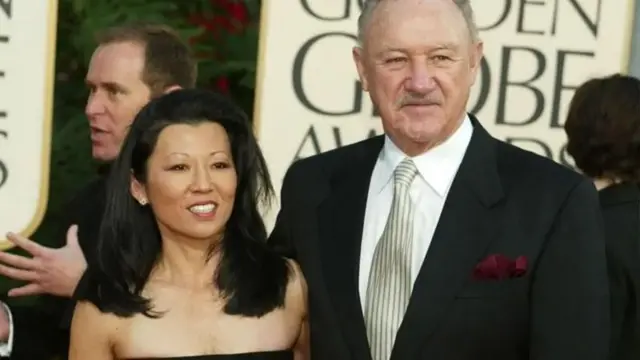 Gene Hackman com a esposa Betsy Arakawa abraçados e sorrindo para foto em evento de gala