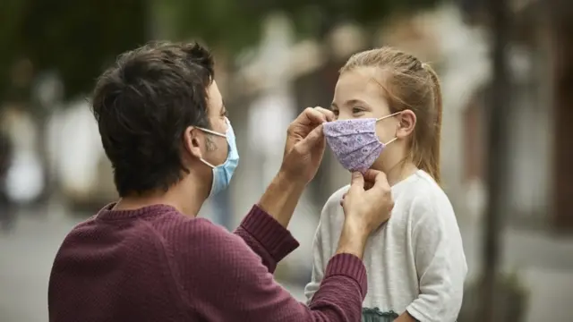 Hombre ajustándole la mascarilla a una niña