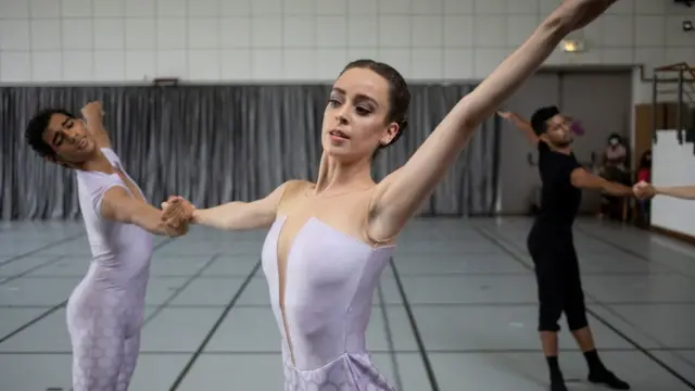 A male and female ballet dancer holding hands while dancing, they are holding a dance pose.