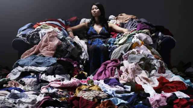 Mujer sentada sobre un desorden de ropa