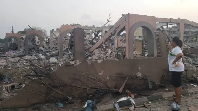 One woman stand dey look di building wey don fall