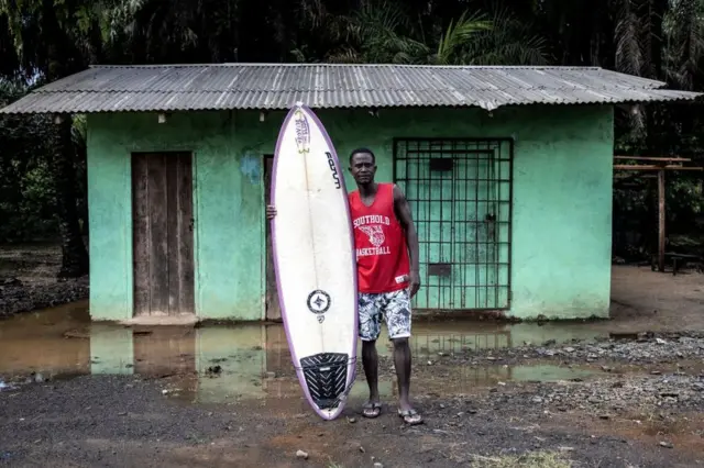 A man poses for a portrait with his surfboard after a morning surfing in Monrovia on November 13, 2021