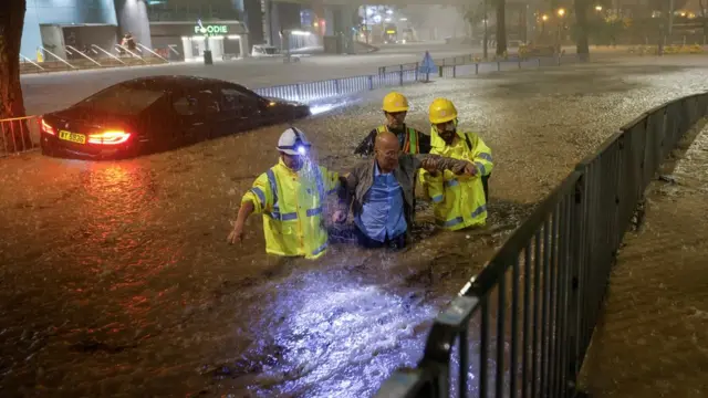 香港某路边疏通沟渠人员搀扶一位被困洪水的司机离开被淹马路（8/9/2023）