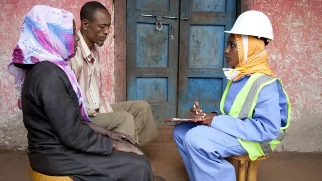 Mosquito eradication worker speaking with a family before spraying their house to prevent malaria.