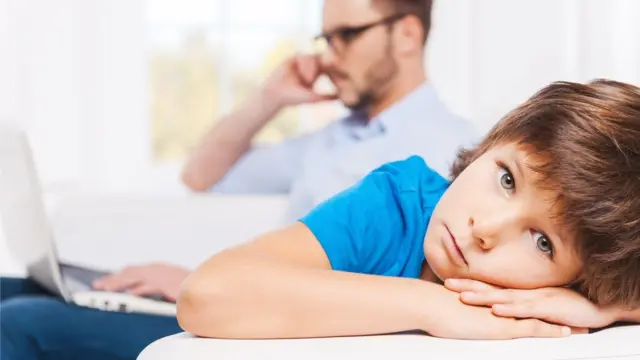 Niña mira a sus padres mientras utilizan sus teléfonos celulares.