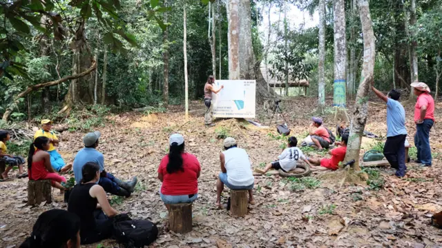 Carlos Magdalena, en la selva amazónica boliviana, con una pancarta apoyada en un árbol, rodeado de pobladores de Motacusal