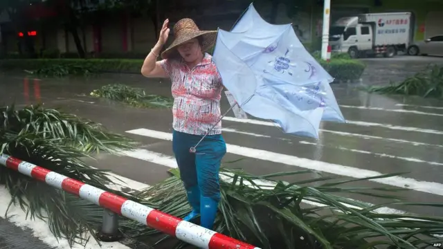 A woman crosses a road with palm tree debris in Yangjiang in China's Guangdong province on 16 September 2018