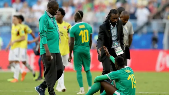Aliou Cissé, avec Cheikh Seck (G) et Omar Daff (D), réconforte Mbaye Niang assis sur la pelouse.