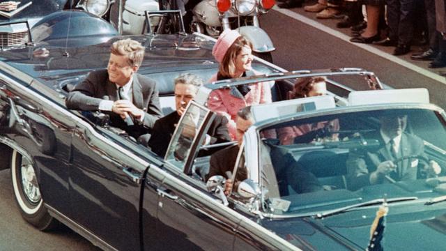Kennedy e a mulher, Jacqueline, sorriem para a multidão que acompanhava o desfile em carro aberto