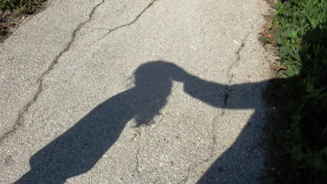Sombra de un adulto tocando en la cabeza a una niña.
