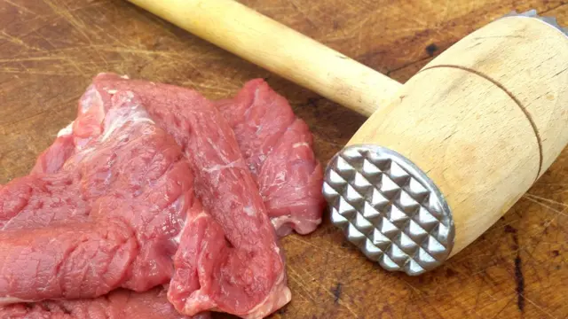 Отбивной кухонный молоток и кусок мяса.