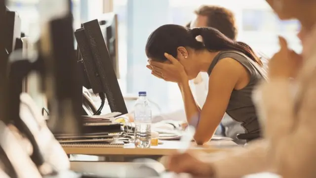 Una mujer, agobiada, con el rostro entre las manos, apoyada en su escritorio