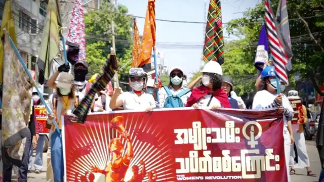 Young protestors hold flags made from sarongs
