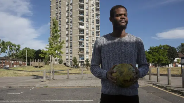Patrick George tenant un ballon de football avec une tour derrière lui