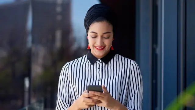 Une jeune femme d'affaires utilisant un smartphone sur le balcon d'un immeuble de bureaux moderne