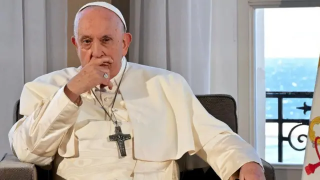 Pope Francis sits on chair leaning his chin on his right hand