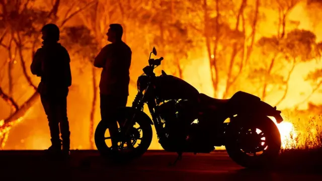 Moradores do lago Tabourie, cercajogo foguete blaze320 quilômetros ao suljogo foguete blazeSydney, na Austrália, observam as chamas devorarem uma floresta.