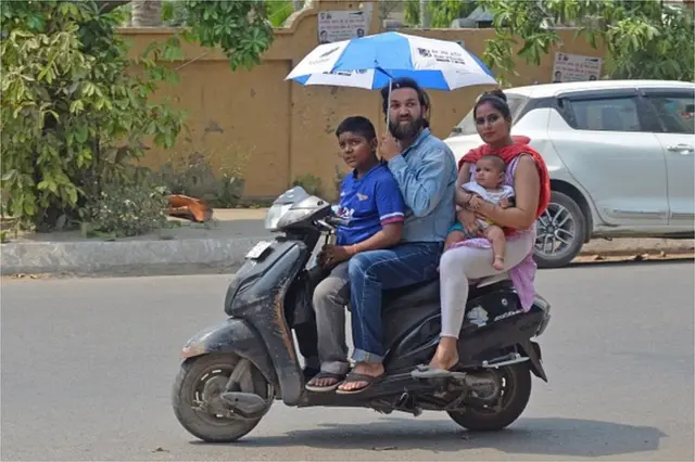 A motorist holds an umbrella while driving a scooter along a road on a hot summer day in Amritsar on May 1, 2022