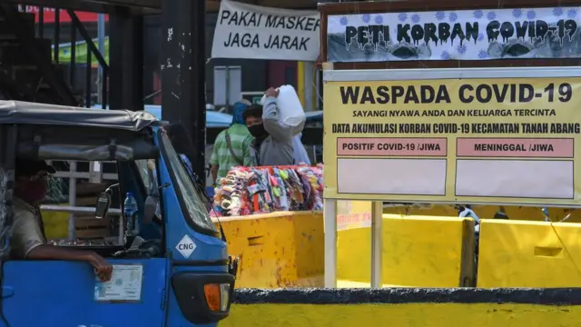 Warga melintasi replika peti mati dan papan himbauan waspada COVID-19 di kawasan Pasar Tanah Abang, Jakarta, Selasa (01/09).
