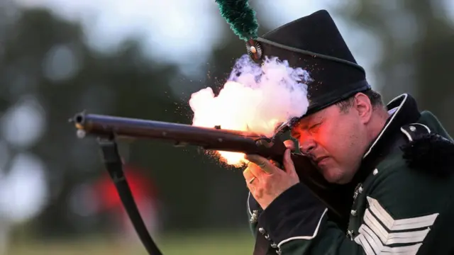 Un hombre con traje de época dispara un mosquete.