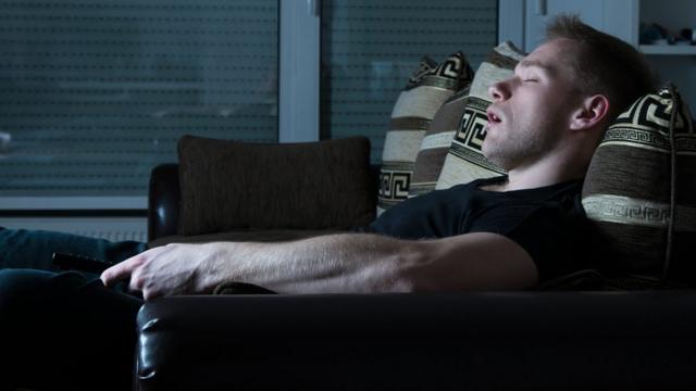 Un hombre duerme frente a un televisor encendido.