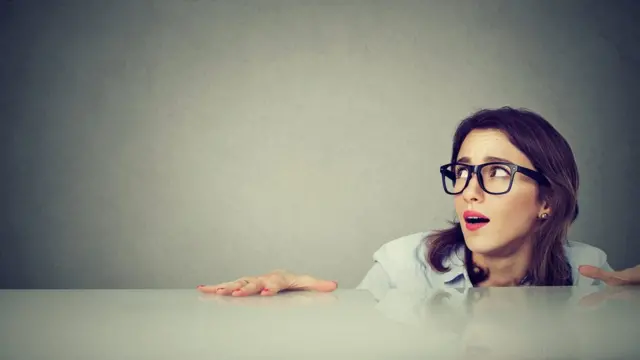 Anxious woman hiding peeking from under the table