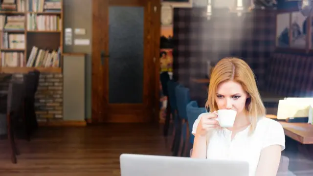 Una joven usando su laptop y tomando un café