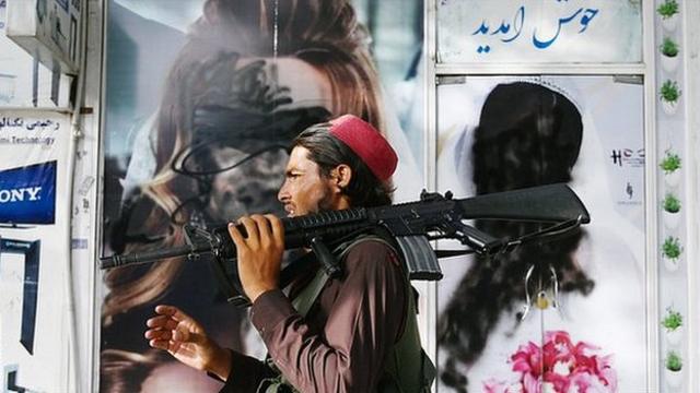 A Taliban fighter walks past a beauty salon with images of women defaced using spray paint in Shar-e-Naw in Kabul on August 18, 2021