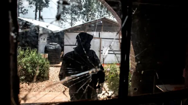 A Police officer stands guard in front of a window riddled with bullet holes in an Ebola treatment centre, which was attacked in the early hours of the morning on 9 March 2019 in Butembo. Wani dan sanda kenan a yayin da ya ke tsaye gaban wata taga wacce ta sha harbe-harben bindiga a cikin wata cibiyar kulla da ebola wacce aka kai wa hari a safiyar ranar tara ga watan Maris 2019 a Butembo.