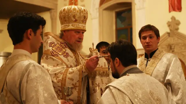 ziyarətçilərin alınlarına "İsa Məsihin suyu"ndan çəkib, xeyir-dua verir.