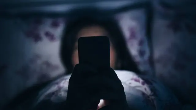 Chica leyendo en la cama un telefono