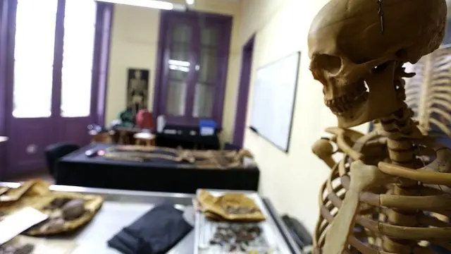 Esqueleto de plástico en primer plano y un laboratorio forense de fondo.