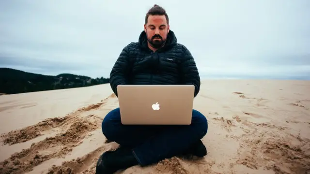 Grant Sabatier usando laptop na praia