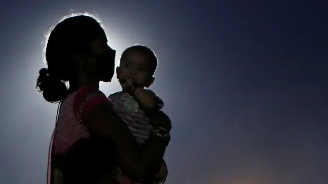 एक माँ अपने बच्चे के साथ घर जाने के लिए बस का इंतज़ार करती हुई