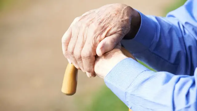 Manos de anciano apoyadas en una bastón.