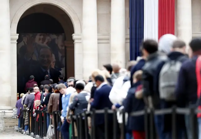 Visitors wait to view the coffin of former French President Jacques Chirac as it lies in state in the Invalides on 29 September 2019.