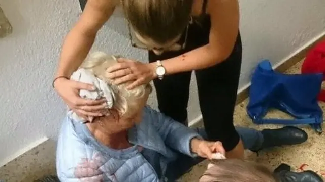 A woman sits injured on a staircase as another person covers her head partially with a cloth, in Barcelona, Spain October 1, 2017