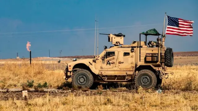 US armoured vehicle drives past a burning gas flare in north-eastern Syria