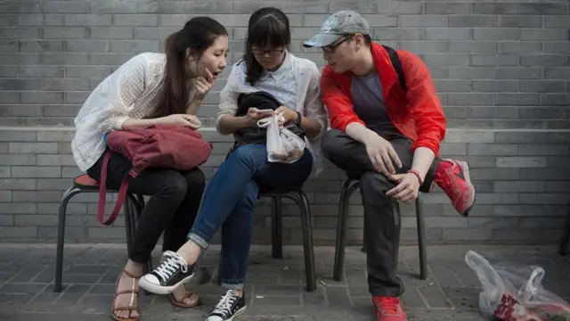 شاب وفتاتان يطالعون هاتفا محمولا