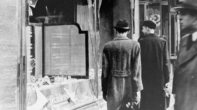 ألمانيون يمرون بجوار نوافذ مهشمة في أعقاب أحداث "ليلة الزجاج المحطم" التي أظهرت للعالم مدى خطورة ألمانيا على اليهود